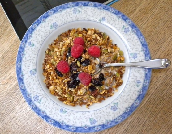 Blue rimmed bowl filled with granola and fruits in milk with a spoon inside the bowl