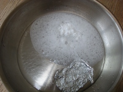 Foaming vinegar and baking soda in stainless steel fry pan and aluminum foil
