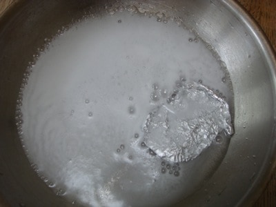 Foaming vinegar and baking soda next to aluminum foil in stainless steel pan