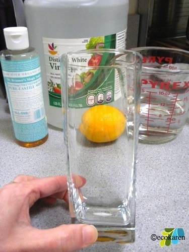 Castile soap, white vinegar, lemon, and 1 cup water in pyrex behind empty glass