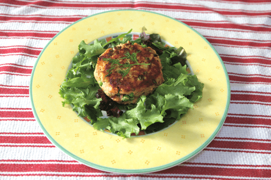 Salmon Cake on a bed of greens on a yellow plate sitting on a red striped towel