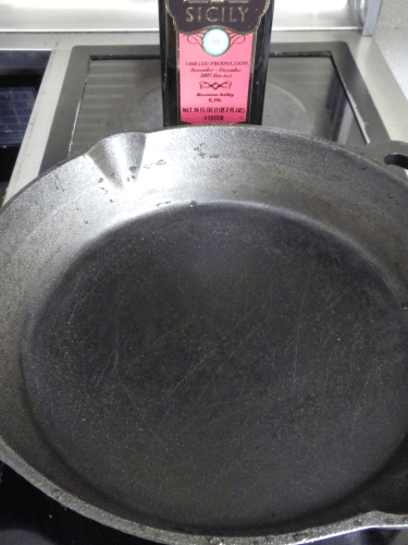 extra virgin olive oil bottle behind cast iron pan