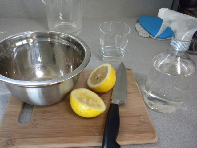 stainless steel bowl, knife, and lemon cut in half on wooden cutting board next to spray bottle