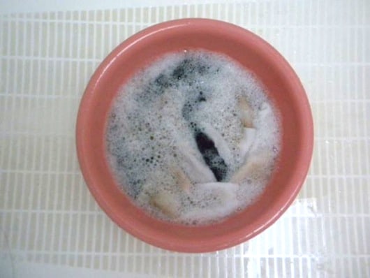 white socks soaking in water, liquid laundry detergent, washing soda, hydrogen peroxide, and lemon juice in a pink bucket in bathtub