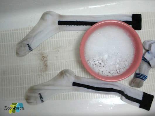 solution of  water, liquid laundry detergent, washing soda, hydrogen peroxide, and lemon juice in pink bowl between cleaned white socks in bathtub