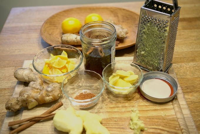 whole and sliced ginger, cinnamon, sliced lemon, mason jar of honey box grater on cutting board