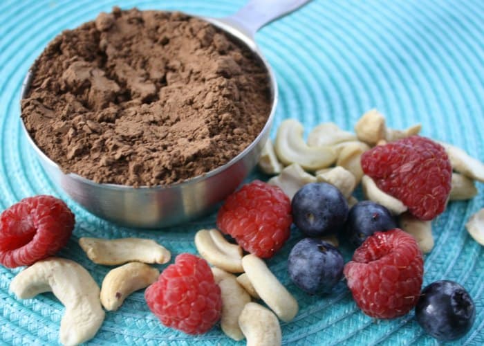 nuts and berries next to cup of cacao powder on blue placemat