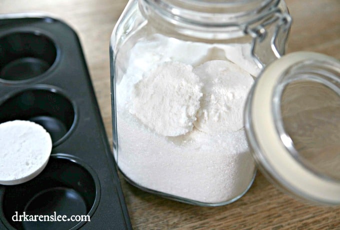 dishwasher detergent tablet on cupcake pan next to glass jar of dishwasher detergent tablets