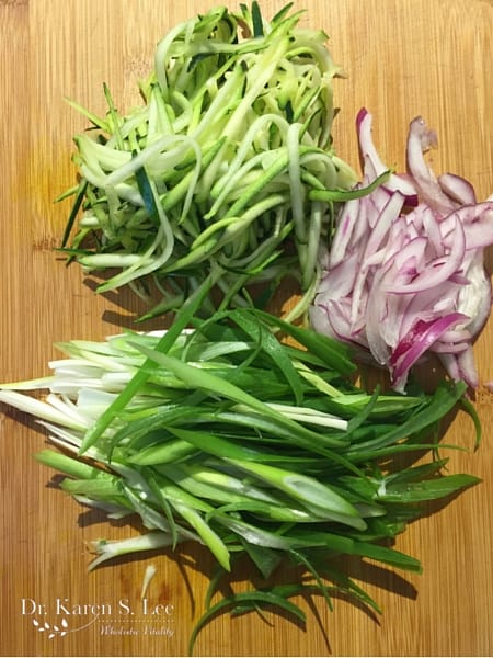 julienned purple onion, zucchini, and scallions on a wooden cutting board