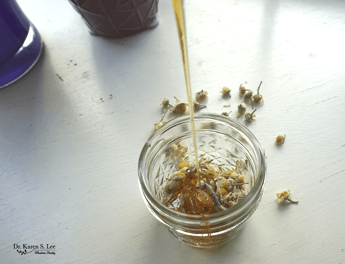 honey pouring into jar of chamomile flowers