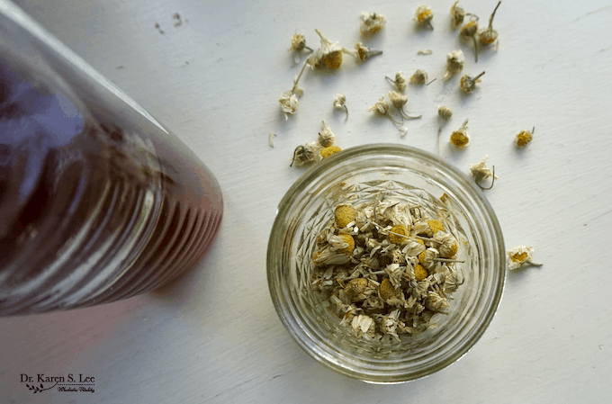 Honey bottle next to glass jar with Chamomile flowers