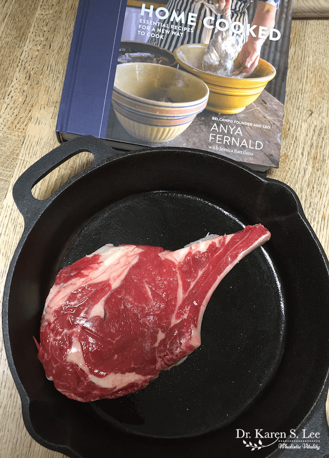 Home Cooked cook book behind raw steak on cast iron pan
