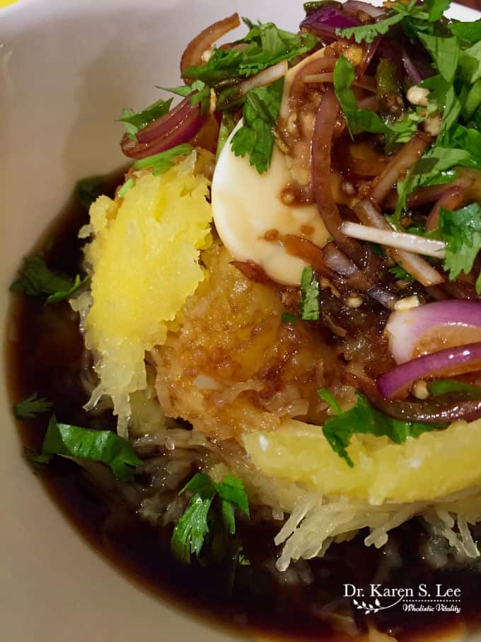 Spaghetti Squash topped with soft boiled egg, cilantro, and purple onion in asian sauce in white bowl