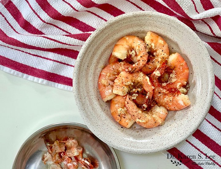 cooked shrimp in a white bowl, shells in a stainless bowl, on red and white striped kitchen towel