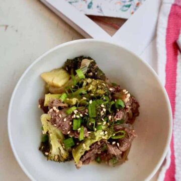 Beef and Broccoli in a while plate with scallions and sesame seeds garnish red striped napkin on the side