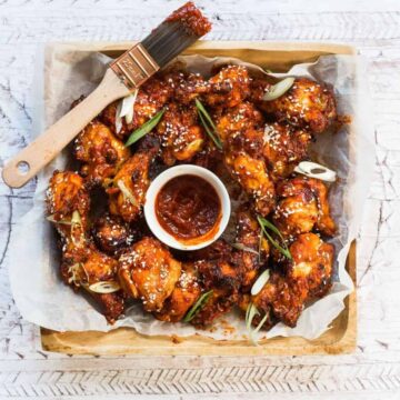 Fried chicken wings with red sauce on a tray with pastry brush with sauce on it