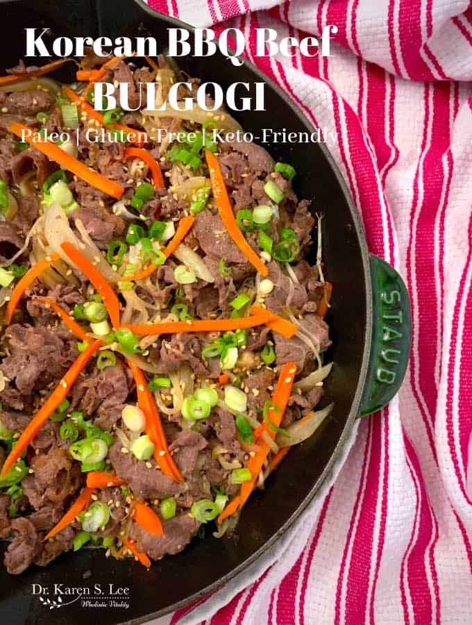 Brown beef slices with slivers of carrots and chopped scallions on a cast iron skillet with red and white stripe napkin in the background