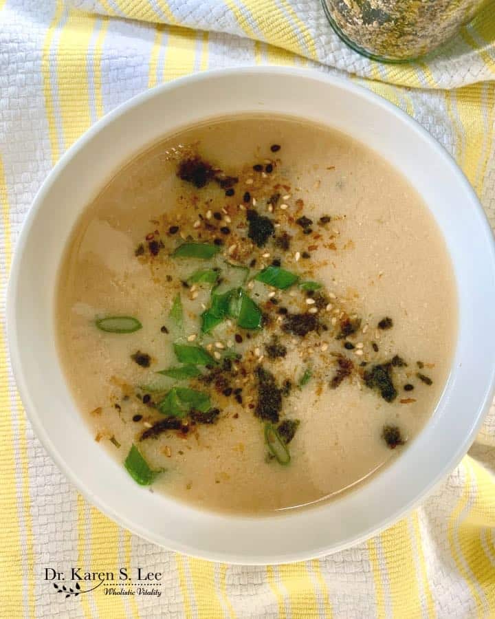 Furikake sprinkled on top of a bowl of miso soup garnished with chopped scallions on yellow and white striped kitchen towel