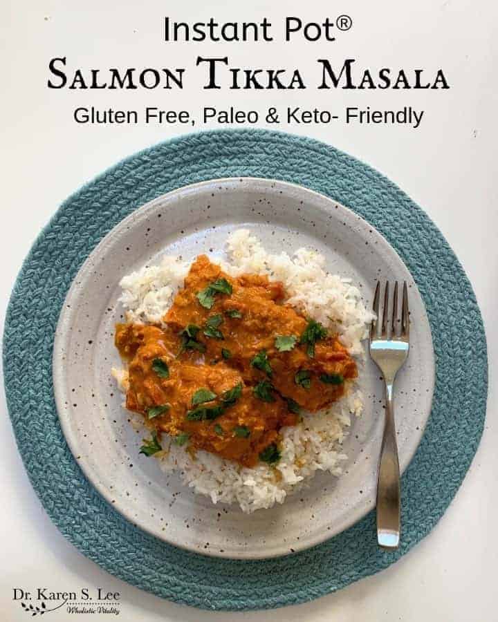 Salmon Tikka Masala in curry sauce over white rice on a speckled whitish plate on a round moss green placemat with a stainless steel fork on the right