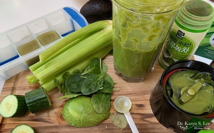 Celery stalks, sliced cucumbers, avocado, Blender jar, and matcha on a brown cutting board