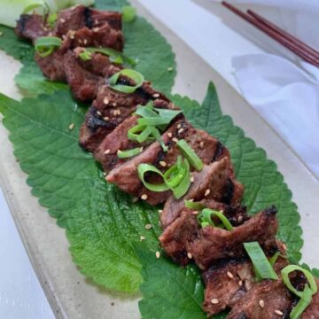 korean bbq galbi pieces on green perilla leaves on a beige platter