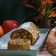 carrot pumpkin roll cake with a slice facing up on a blue rectangular plate with fall decoration around it