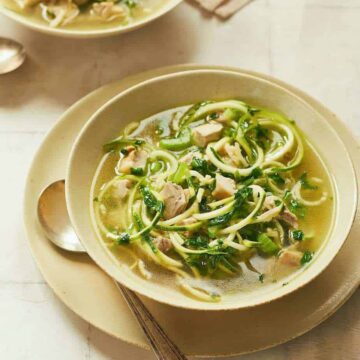 chicken zoodle soup in beige soup bowl on platter with a spoon