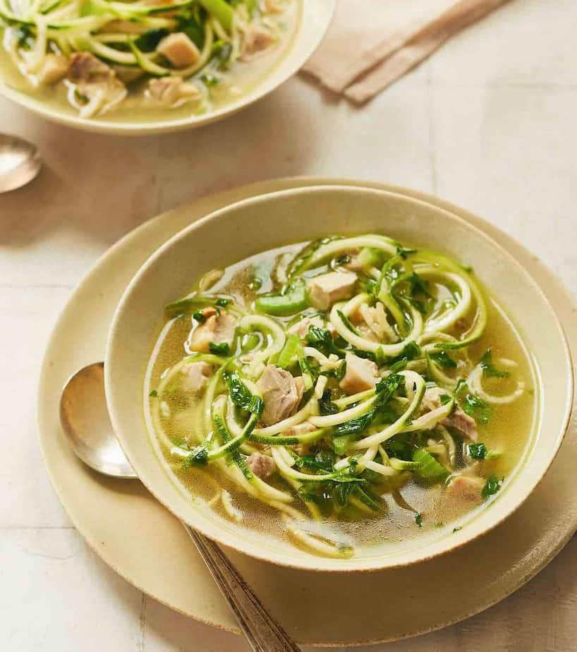chicken zoodle soup in beige soup bowl on platter with a spoon