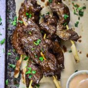Beef skewers on parchment paper with pink sauce on side