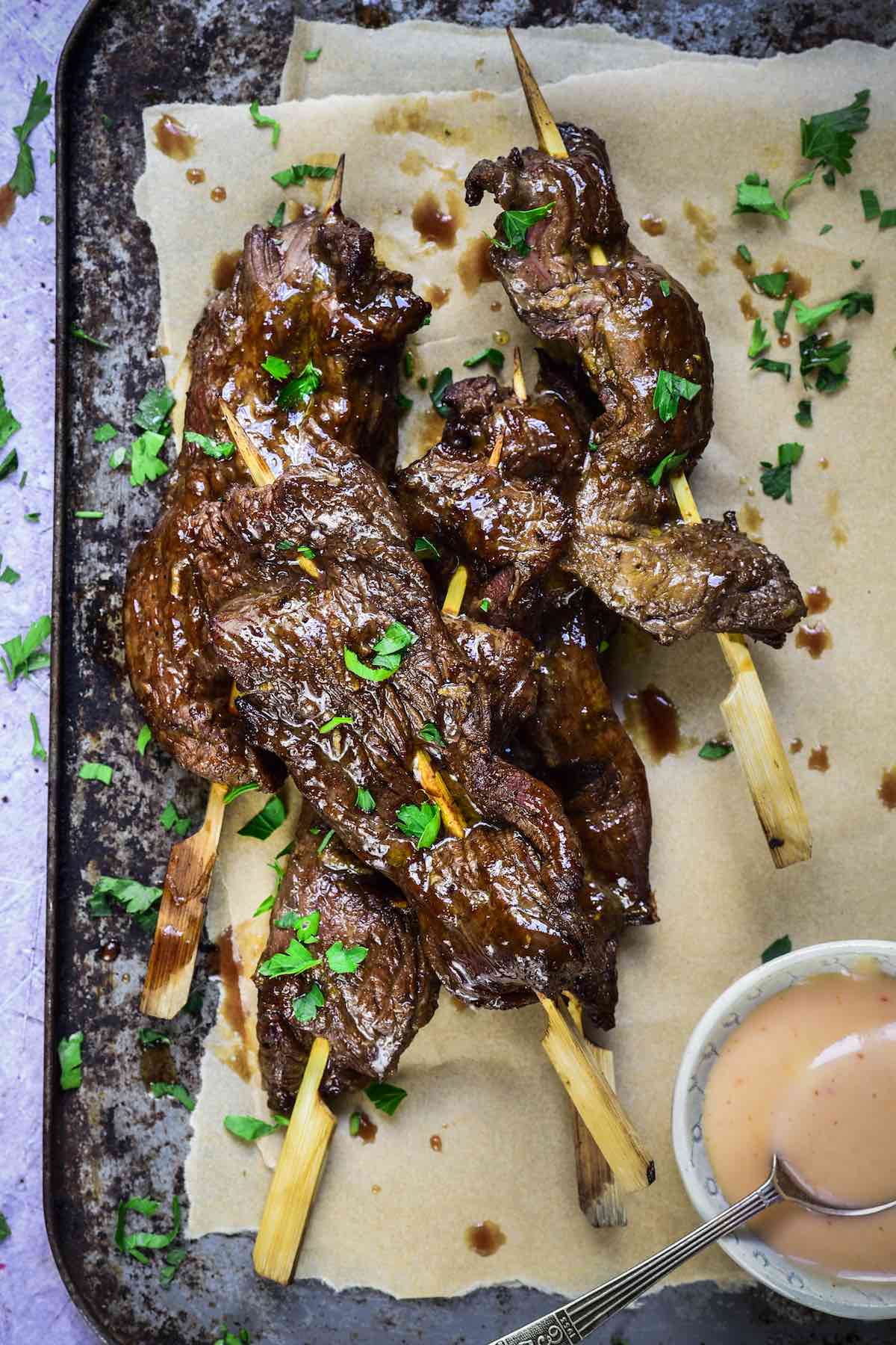 Beef skewers on parchment paper with pink sauce on side