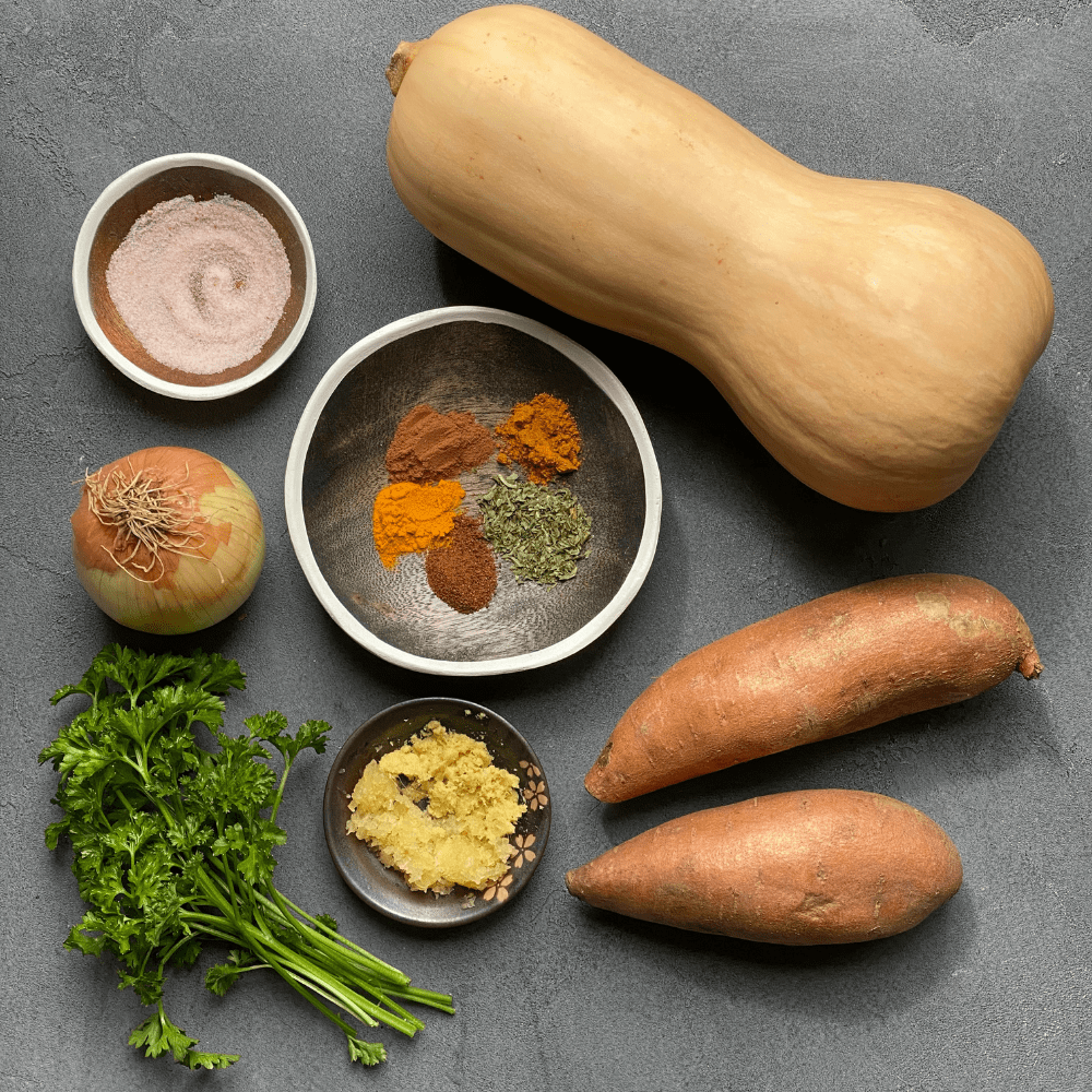 butternut squash, sweet potatoes, 3 plates of herbs and spices, onion, and parsley on grey background