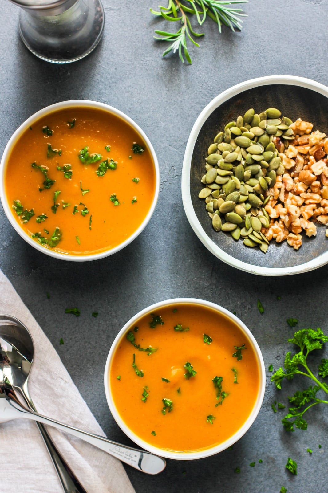 2 bowls of orange colored soup with green garnish next to a plate with seeds