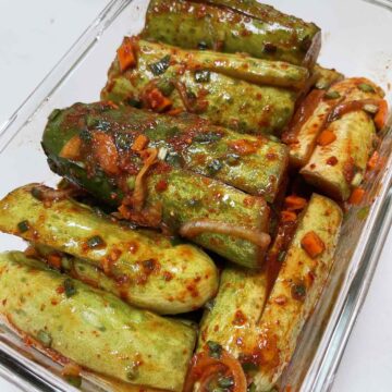 cucumbers stuffed with red pepper flakes, carrots, and onions in a glass container